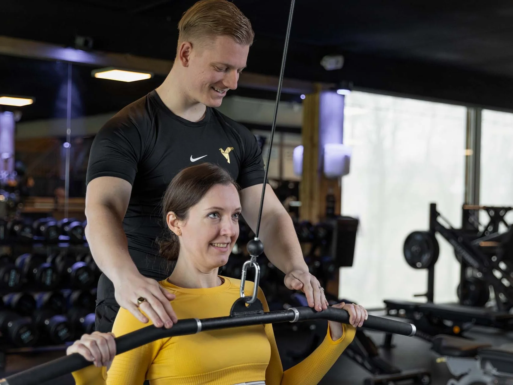 Personal trainer van Club12 begeleidt een klant bij een oefening aan de latmachine