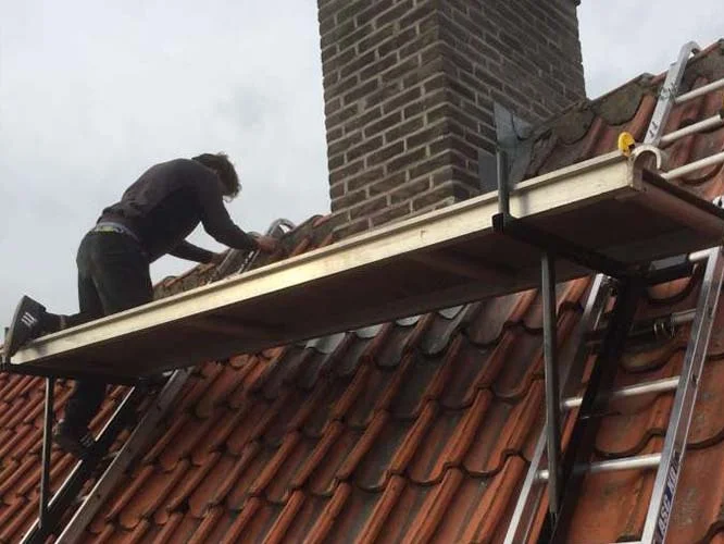 Dakdekker van DKH werkt vanaf een steiger aan een pannendak naast de schoorsteen