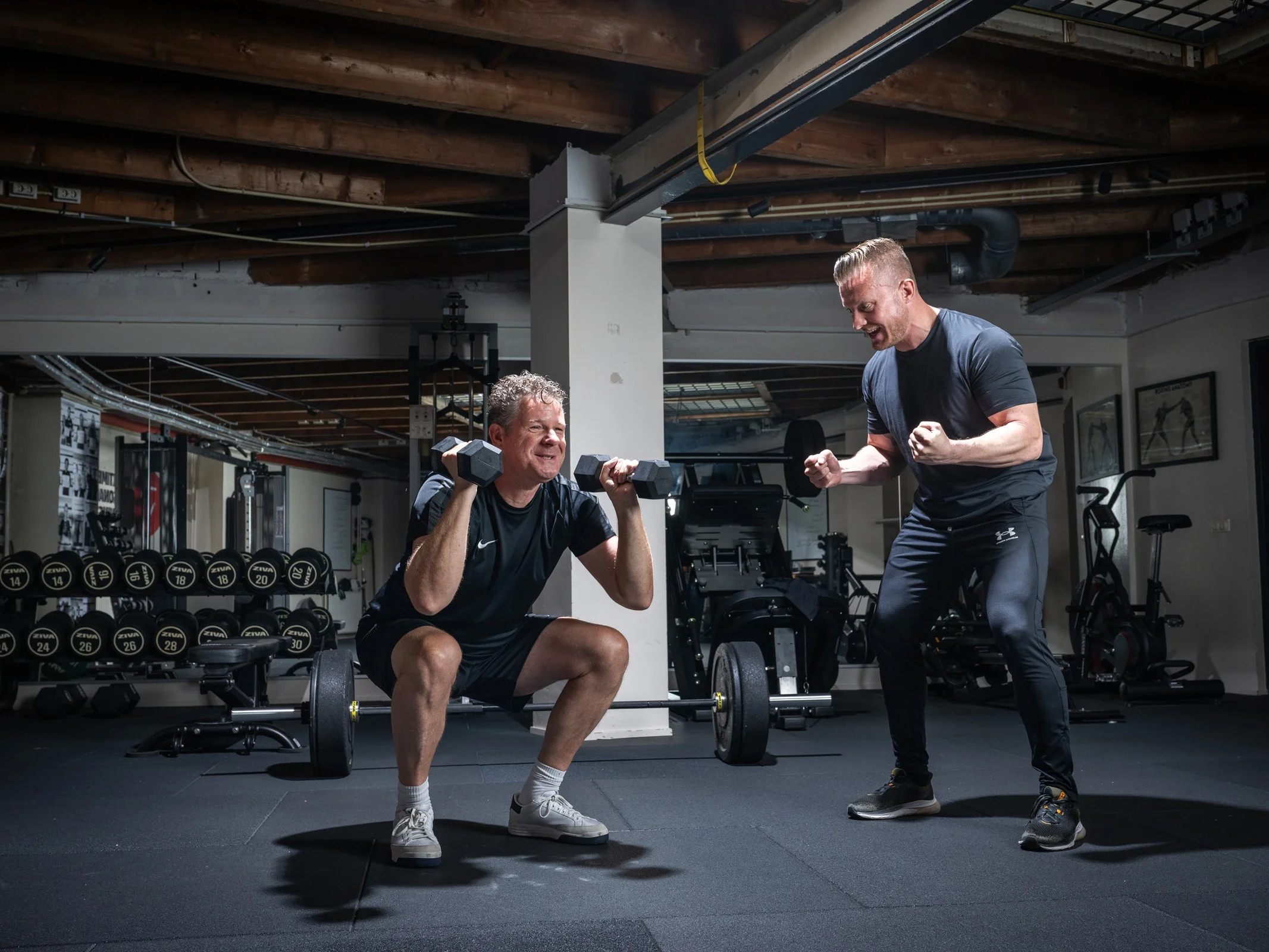 Personal trainer van PeakTime moedigt een klant aan die met dumbbells squat in de studio in Utrecht