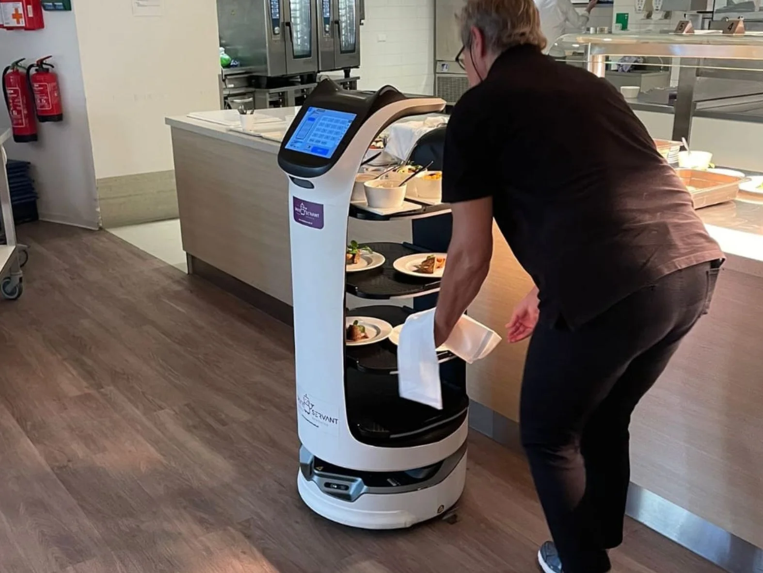 Medewerker zet borden met eten op een serveerrobot van Smart Servant in een bedrijfskeuken